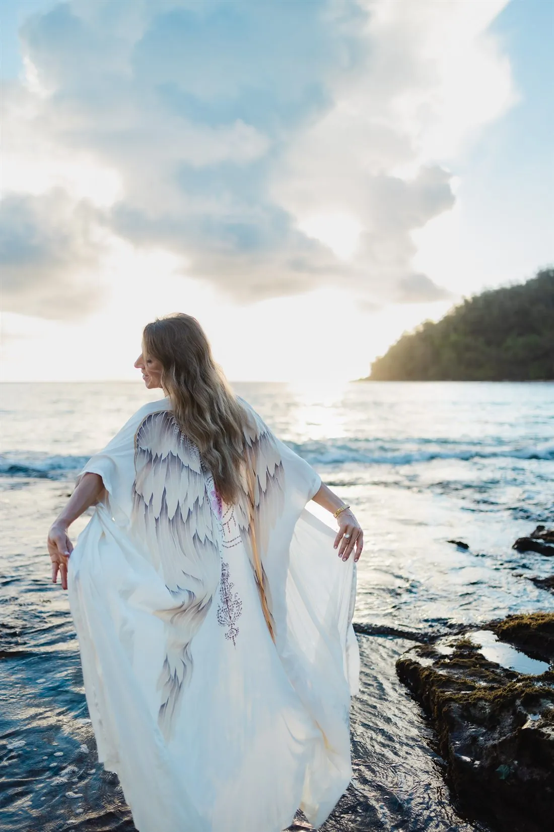 Christine Mira Rose in a white winged robe at the ocean's edge
